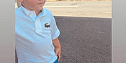 Emilio a rejoint le concours — aidez-le/la à gagner de superbes lots ! toddler, child, white_polo, blue_shorts, white_shoes, asphalt, outdoor, construction_truck, vehicle, short_hair, side_view, casual_clothing, sunny_day, standing, young_boy, curious_expression, fence, industrial_area, daylight, footwear