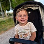 child, toddler, stroller, tshirt, smiling, outdoor, park, greenery, happy, cute, face, short_hair, seat, daylight, person, young, nature, casual_clothing, relaxing, portrait