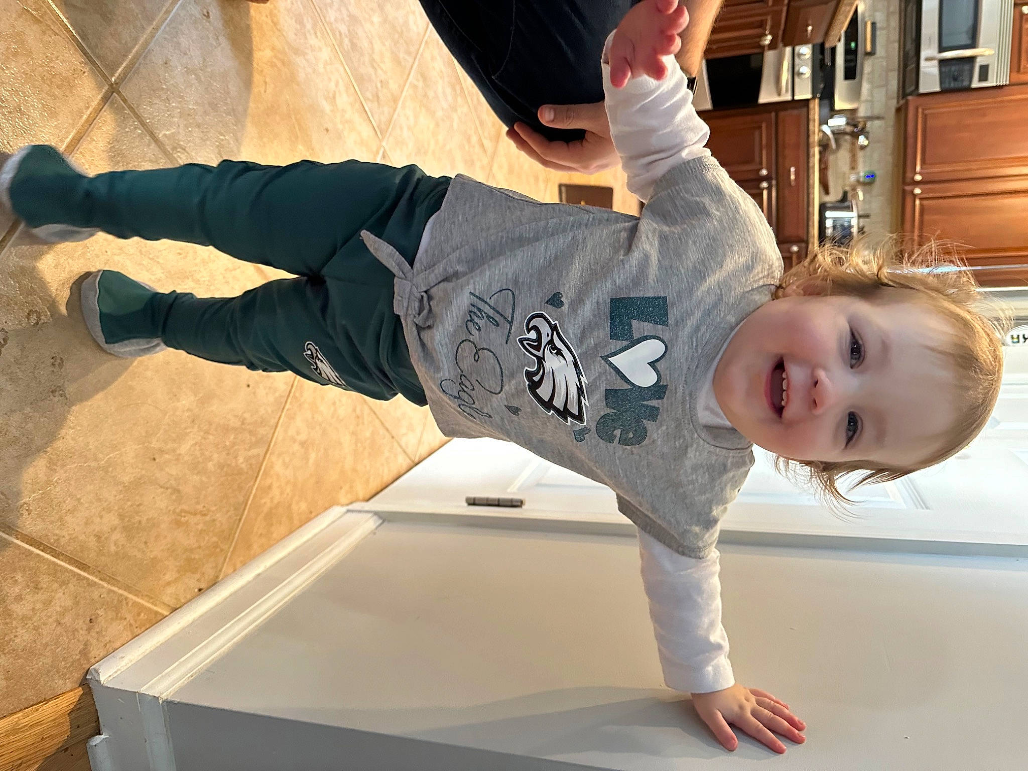 Hadley is registered to the contest to win money with this photo: baby_toddler_clothing, balance, cabinetry, child, denim, flooring, fun, happy, joint, joy, knee, leg, outdoor_shoe, person, sitting, sleeve, smile, sneakers, t_shirt, toddler
