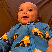 Wyatt joined the competition — help win amazing prizes! baby, infant, child, smiling, happy, portrait, close_up, face, eyes, open_mouth, indoors, seated, blue_outfit, patterned_clothing, yellow_designs, brown_background, cushion, cozy, looking_up, photography