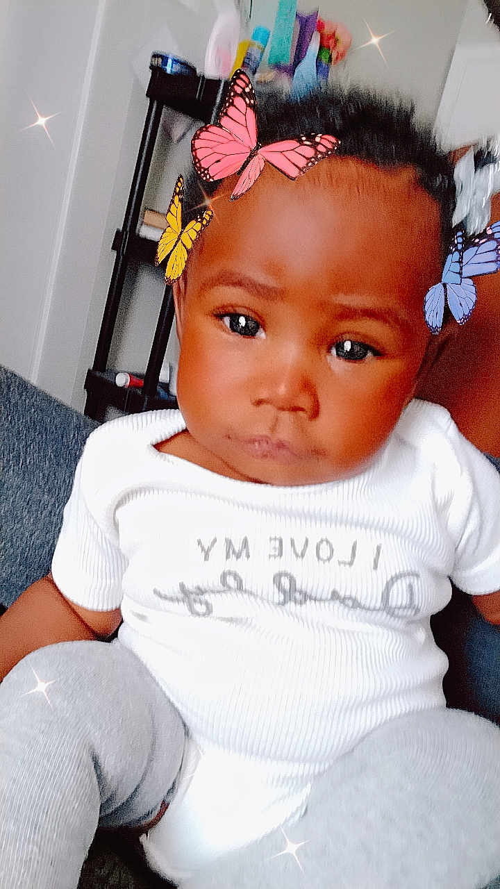 Mi'Ky'ealah America joined the competition — help win amazing prizes! baby, child, indoor, butterfly_filter, digital_filter, white_shirt, gray_pants, sitting, face, expression, furniture, shelf, toy, person, cute, portrait, head, room, casual, closeup