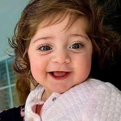 Sophia is registered to the contest to win money with this photo: baby, child, smile, happy, face, portrait, indoor, clothing, quilted_jacket, curly_hair, person, hand, holding, cute, infant, young_child, bright_eyes, expression, warm, soft_lighting