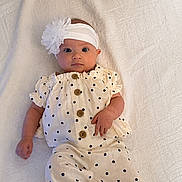 Aubrey is registered to the contest to win money with this photo: baby, infant, polka_dot, white_headband, flower_accessory, wooden_buttons, cream_clothing, lying_down, blanket, soft_texture, cute, portrait, child, small_hands, blue_eyes, casual_outfit, indoor, comfortable, adorable, looking_at_camera