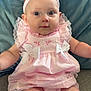 Delilah is registered to the contest to win money with this photo: baby, infant, pink_dress, headband, bows, sitting, cushion, blue_background, cute, portrait, child, indoors, soft_fabric, closeup, smiling, happy, young_child, plush, adorable, person