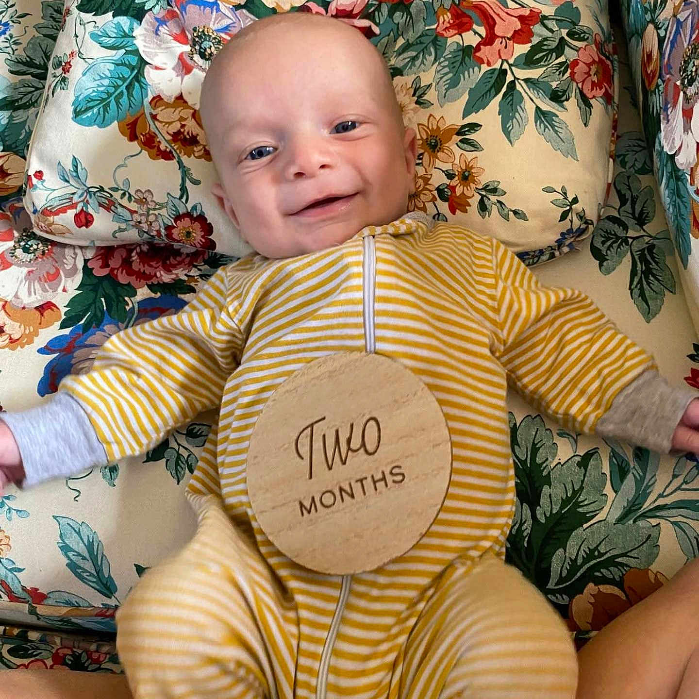 Tower is registered to the contest to win money with this photo: baby, child, cushion, cute, expression, face, floral_pattern, happy, head, indoor, infant, lying_down, newborn, onesie, person, pillow, skin, smile, wooden_sign, yellow_striped_clothing