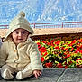 baby, child, hooded_sweater, sitting, stone_ledge, flowers, red_flowers, mountain, lake, outdoor, nature, cute, smiling, person, scenic, greenery, winter_clothing, portrait, daylight, casual