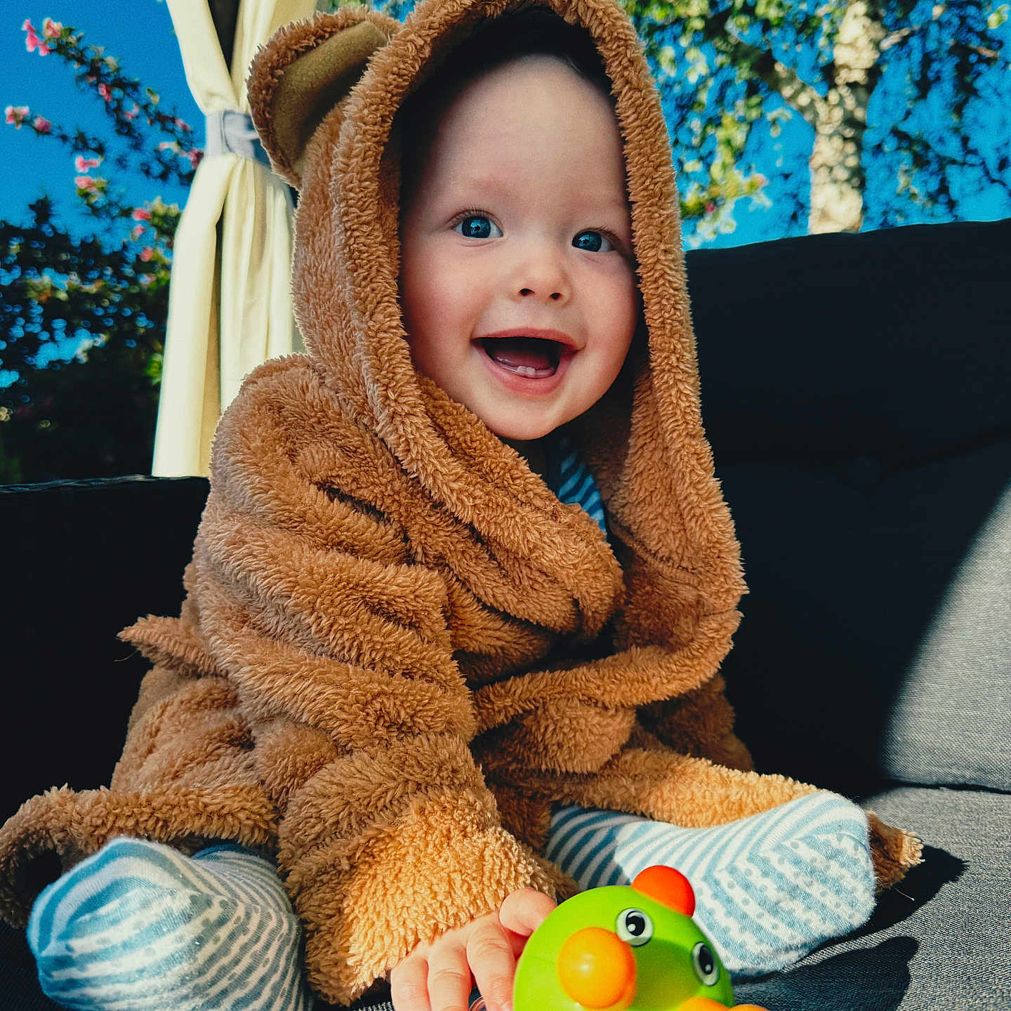 Markas is registered to the contest to win money with this photo: baby, blue_sky, bright_colors, child, couch, cute, fuzzy_clothing, greenery, happy, hooded_jacket, infant, nature, outdoor, playful, portrait, smiling, striped_socks, sunlight, toddler, toy
