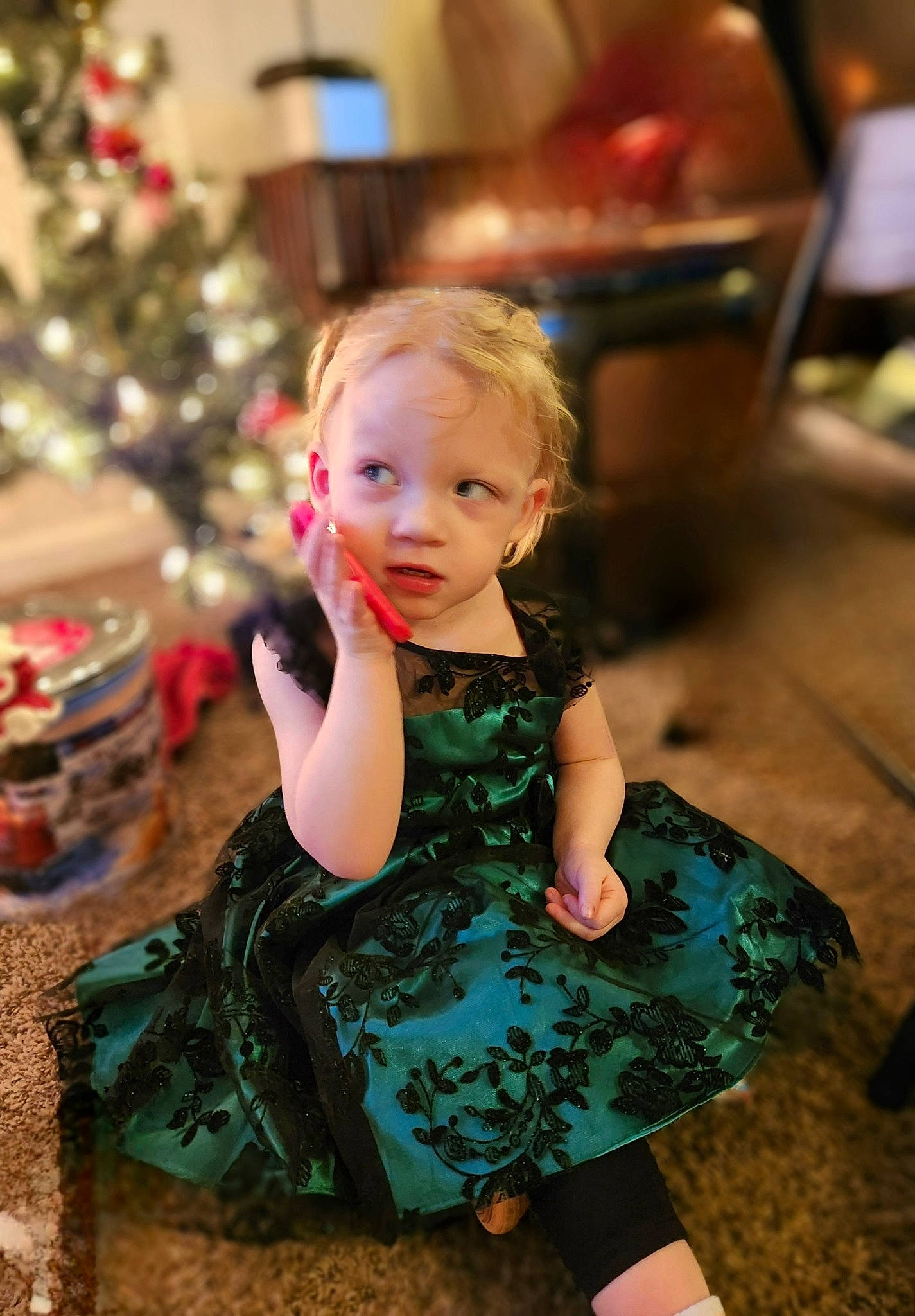 Willow is registered to the contest to win money with this photo: baby_toddler_clothing, child, christmas_decoration, christmas_tree, day_dress, dress, event, facial_expression, fashion_design, formal_wear, fun, hairstyle, happy, holiday, iris, one_piece_garment, person, sitting, standing, toddler