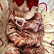 Willow is registered to the contest to win money with this photo: baby, sleeping, pacifier, red_bow, floral_onesie, blanket, rainbow_pattern, infant, cute, peaceful, child, soft_texture, cozy, hand, face, headwear, apparel, rest, indoors, portrait