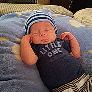 Bryson is registered to the contest to win money with this photo: baby, newborn, infant, sleeping, closed_eyes, striped_hat, blue_blanket, onesie, little_one_text, hands, peaceful, cozy, striped_pants, pillow, nursery, home_interior, sofa, blanket_stars, sleeping_pose, portrait