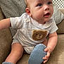 Rueben is registered to the contest to win money with this photo: baby, infant, child, couch, blanket, blue_eyes, onesie, teddy_bear_patch, booties, soft_toys, indoor, portrait, cute, smiling, seated, cozy, furniture, hand, face, expression