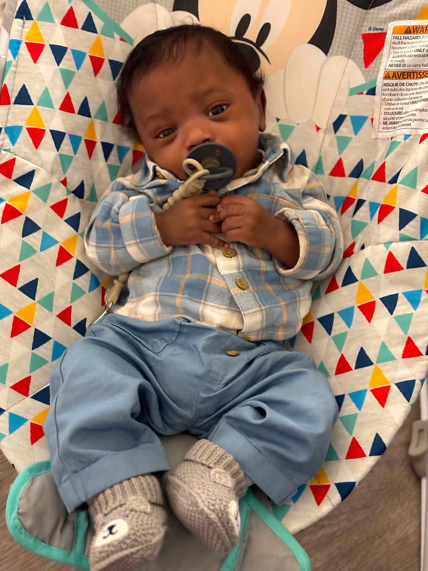 Adrian Hyman is registered to the contest to win money with this photo: baby, baby_accessory, baby_seat, blue_clothing, blue_pants, child, colorful_pattern, comfort, cute, footwear, hand_holding, indoor, infant, knit_booties, pacifier, plaid_shirt, portrait, resting, triangle_pattern, young