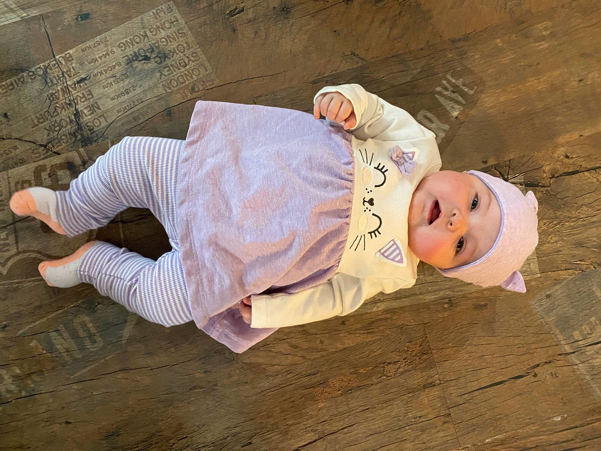 Ashley a rejoint le concours — aidez-le/la à gagner de superbes lots ! baby, baby_toddler_clothing, child, floor, flooring, fun, happy, hardwood, hat, headwear, human_leg, linens, pattern, person, sitting, sleeve, smile, t_shirt, toddler, uniform