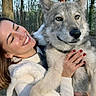 animal, casual_clothing, daylight, dog, forest, friendship, fur, happy, holding, human, nature, outdoor, pet, portrait, red_nails, smiling, tree_trunk, trees, wolf_like_dog, woman