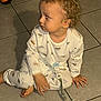 toddler, child, pajamas, toy, floor, tile, indoor, curious, sitting, barefoot, clothing, young_child, person, baby, cute, curly_hair, looking_away, shadow, playtime, comfort