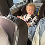 Ewen a rejoint le concours — aidez-le/la à gagner de superbes lots ! toddler, child, car_seat, car_interior, smiling, curly_hair, seatbelt, window, parked_cars, sunlight, person, clothing, jacket, fabric, seat, headrest, safety, happy, vehicle, transportation