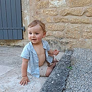 Lucas a rejoint le concours — aidez-le/la à gagner de superbes lots ! toddler, child, sitting, stone_floor, gravel, blue_shirt, beige_shorts, bare_chest, curious, happy, outdoor, stone_wall, door, hand, feet, person, portrait, young_child, casual_clothing, daylight