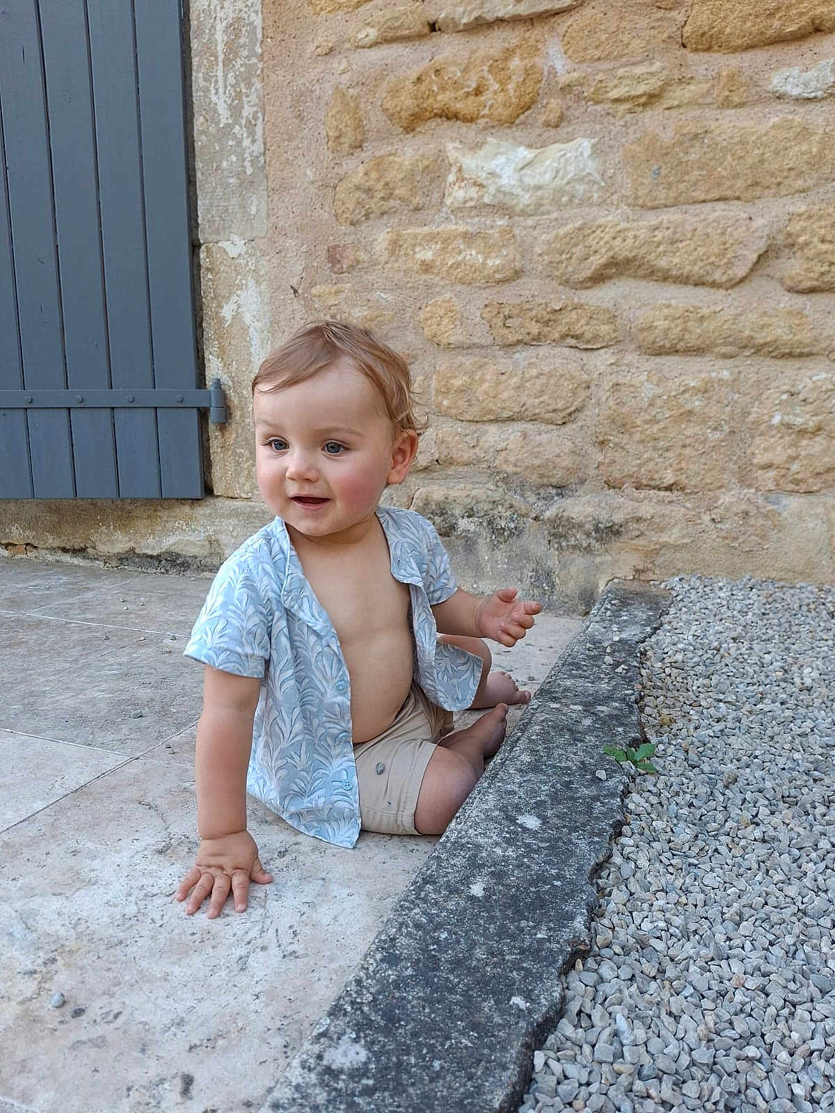 Lucas a rejoint le concours — aidez-le/la à gagner de superbes lots ! toddler, child, sitting, stone_floor, gravel, blue_shirt, beige_shorts, bare_chest, curious, happy, outdoor, stone_wall, door, hand, feet, person, portrait, young_child, casual_clothing, daylight