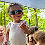 toddler, sunglasses, white_onesie, child, outdoor, trees, forest, canopy, smile, curly_hair, person, adult, background, nature, summer, shade, happy, casual, family, fun