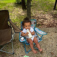 Meeko is registered to the contest to win money with this photo: toddler, child, outdoor, grass, tree, gravel, bottle, milk, chair, folding_chair, curly_hair, white_clothing, wipes, nature, park, daytime, relaxing, barefoot, cute, peaceful