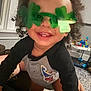 child, toddler, glasses, green, shamrock, smile, curly_hair, indoor, toy, playful, shirt, patch, happy, face, person, candid, cheerful, home, background, baby