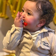 Anas a rejoint le concours — aidez-le/la à gagner de superbes lots ! baby, beige_jacket, blurred_background, candid, child, closeup, clothing, curly_hair, ear, gaze, gold_balloon, hand_on_mouth, indoor, pacifier, party_decoration, portrait, rosy_cheeks, sitting, soft_lighting, toddler