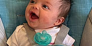 Poppy is registered to the contest to win money with this photo: baby, baby_seat, child, clothing, comfort, cushion, cute, face, happy, head, human, indoors, infant, pacifier, pink_pants, smiling, straps, sun_rainbow_design, toy, white_shirt
