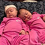 baby, sleeping, pink_clothing, nike_logo, twin_babies, infant, cushion, patterned_background, peaceful, cute, indoor, soft_lighting, relaxing, matching_outfits, newborn, small_hands, resting, portrait, child, cozy