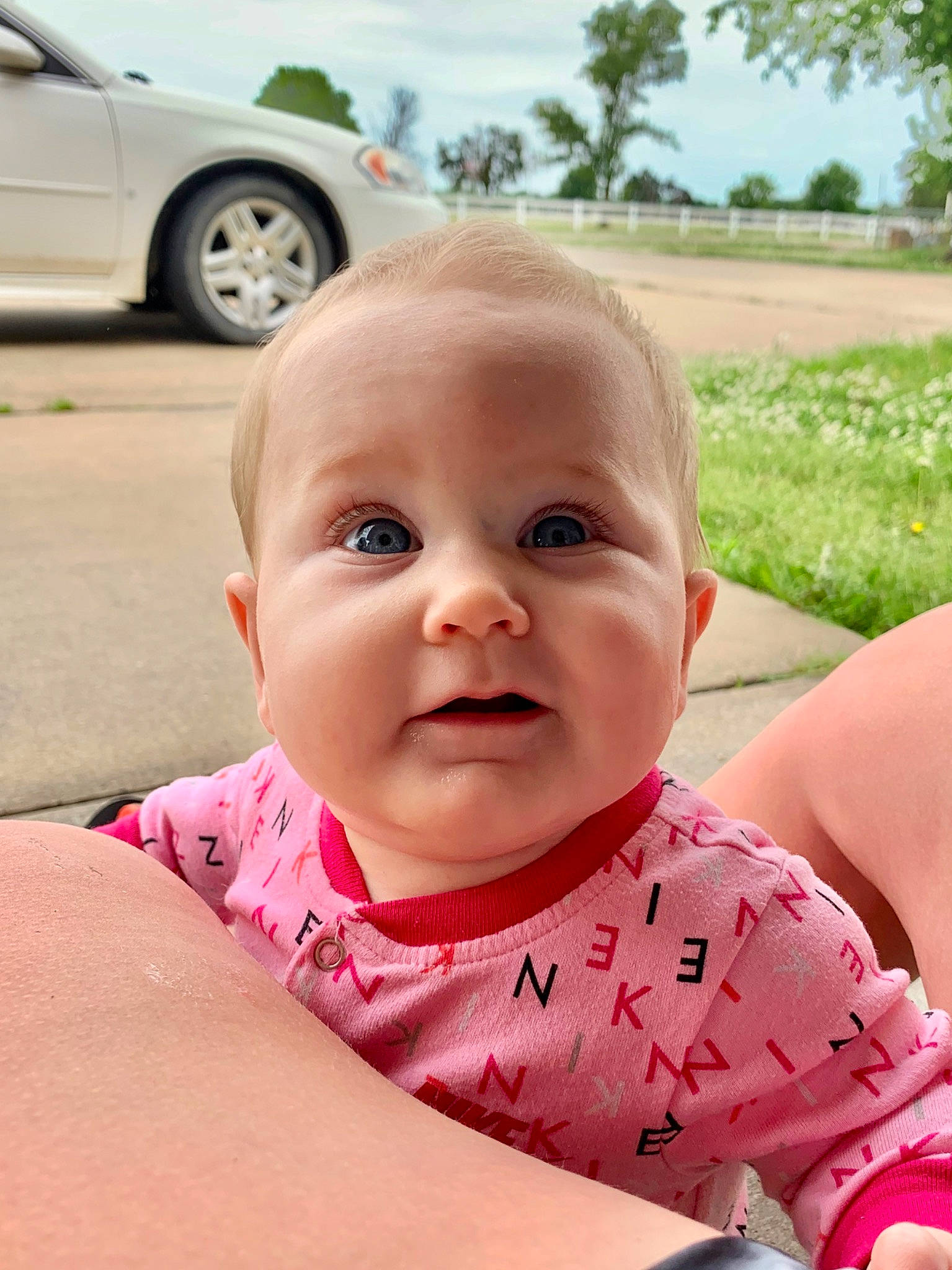 Baker is registered to the contest to win money with this photo: baby, beauty, car, cheek, child, eye, face, facial_expression, grass, head, lip, mouth, nose, person, pink, plant, skin, smile, summer, toddler