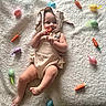 baby, child, bunny_ears, costume, carrot, toy, easter_eggs, blanket, infant, cute, lying_down, playful, soft_texture, decorations, holiday_theme, smiling, indoors, colorful, happy, small_child