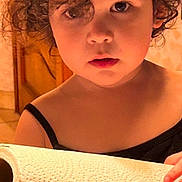 Sofia participe au concours pour gagner de l'argent avec cette photo : child, toddler, curly_hair, paper_towel, holding, indoor, portrait, face, eyes, hands, black_clothing, skin, expression, young, cute, curiosity, home, floor_tiles, door, wall