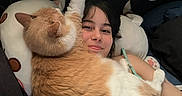 King is registered to the contest to win money with this photo: animal, arm, bed, casual, cat, comfort, cozy, cute, feline, human_face, indoor, lying_down, orange_cat, person, pet, pillow, relaxing, resting, smiling, white_cat