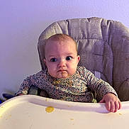 Renesmee is registered to the contest to win money with this photo: baby, high_chair, food, messy, face, table, child, expression, indoor, clothing, hand, wall, curious, sitting, feeding, infant, tray, purple_light, young_child, portrait