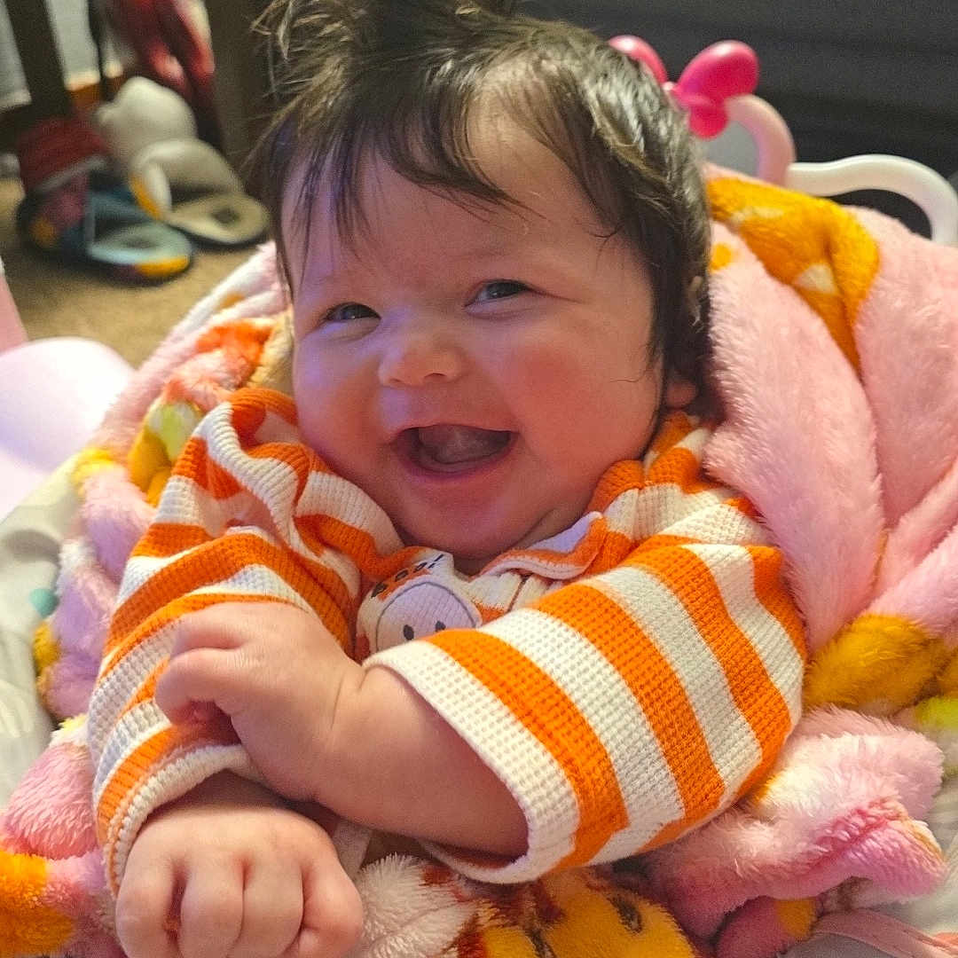 Calliope joined the competition — help win amazing prizes! baby, infant, child, smiling, happy, portrait, indoor, blanket, cozy, striped_clothing, orange, colorful, toy, chair, seated, face, hair, hands, nursery, candid