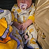 baby, infant, child, pacifier, couch, blanket, pillow, pajamas, sleepwear, sitting, lying_down, portrait, face, eyes, indoors, home, soft_furnishings, plush_toy, cozy, photograph