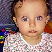 Louisa a rejoint le concours — aidez-le/la à gagner de superbes lots ! baby, child, face, eyes, expression, toys, colorful, patterned_background, clothing, floral, indoor, portrait, young_child, curly_hair, looking_at_camera, play_area, soft_lighting, cuteness, infant, sitting