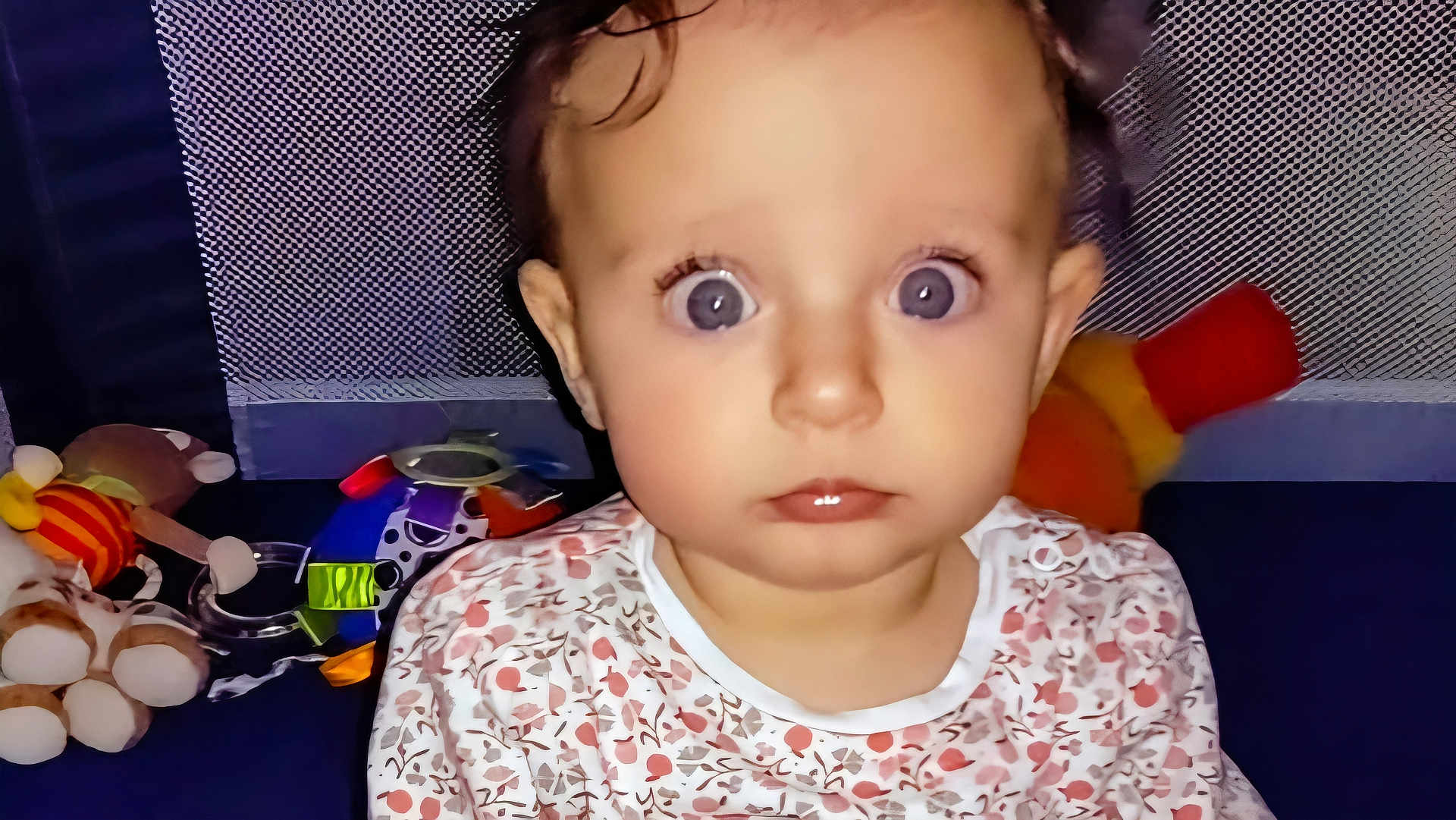 Louisa a rejoint le concours — aidez-le/la à gagner de superbes lots ! baby, child, face, eyes, expression, toys, colorful, patterned_background, clothing, floral, indoor, portrait, young_child, curly_hair, looking_at_camera, play_area, soft_lighting, cuteness, infant, sitting