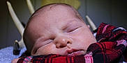 Sutton is registered to the contest to win money with this photo: antlers, baby, background_blur, blue_blanket, child, close_up, cozy, cute, face, indoors, newborn, peaceful, plaid_shirt, portrait, red_clothing, resting, sleeping, soft_texture, warm_lighting, wooden_deer_head