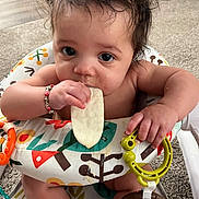 Kai is registered to the contest to win money with this photo: baby, infant, teething_toy, food, high_chair, colorful, indoor, carpet, braclet, cute, messy, drool, child, person, feeding, hands, face, hair, eyes, sitting