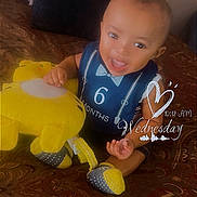 Nisaiah is registered to the contest to win money with this photo: baby, bedspread, blue_outfit, child, cute, day_of_week, happy, home, indoors, infant, patterned_bedspread, plush_toy, portrait, sitting, smiling, soft_focus, text_overlay, time_stamp, yellow_toy, young_child
