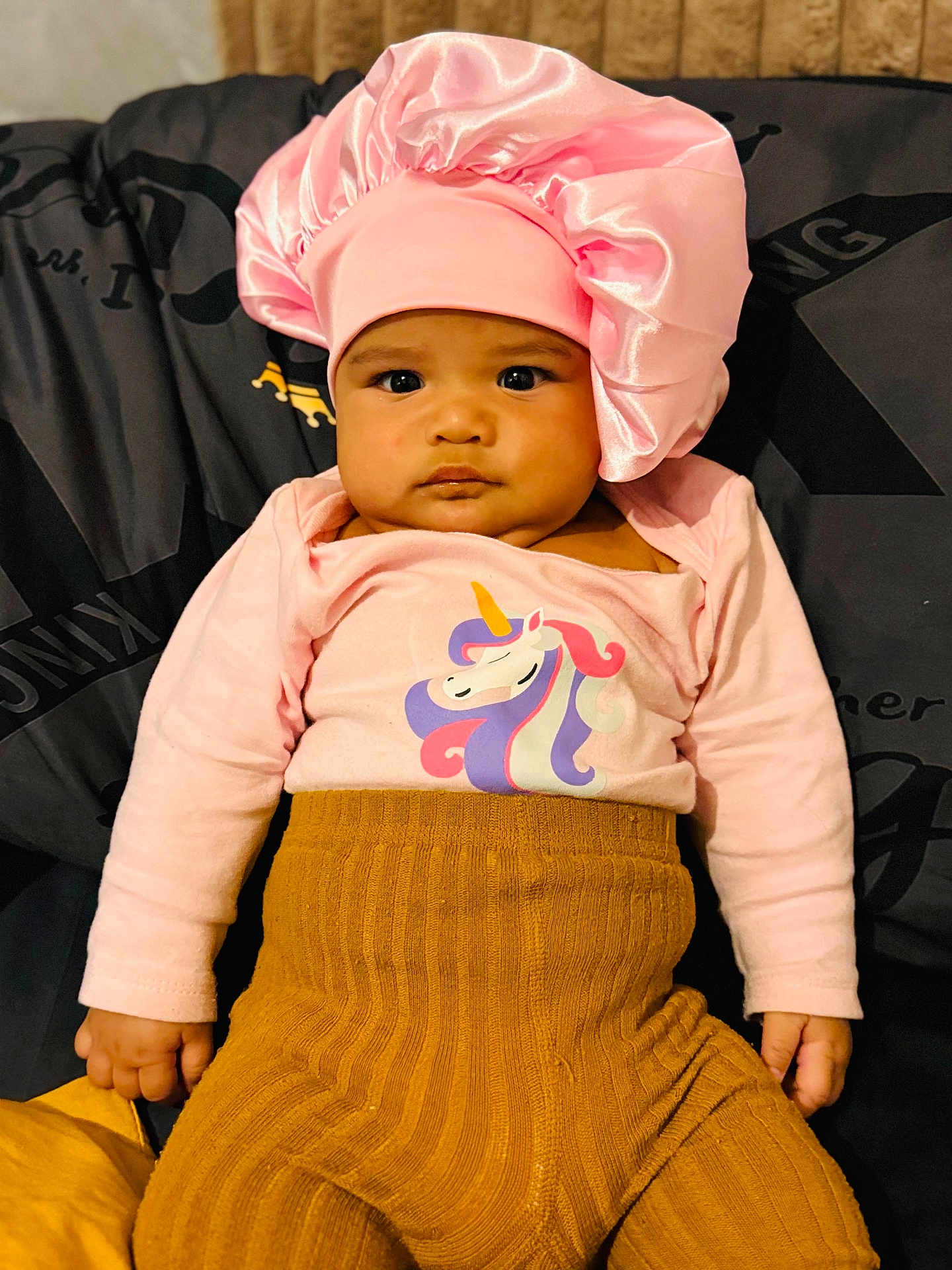 Toahina a rejoint le concours — aidez-le/la à gagner de superbes lots ! baby, child, pink_bonnet, unicorn_shirt, mustard_pants, knitwear, cushion, seated, indoors, portrait, cute, serious_expression, face, hand, clothing, infant, person, headwear, fabric, soft_texture