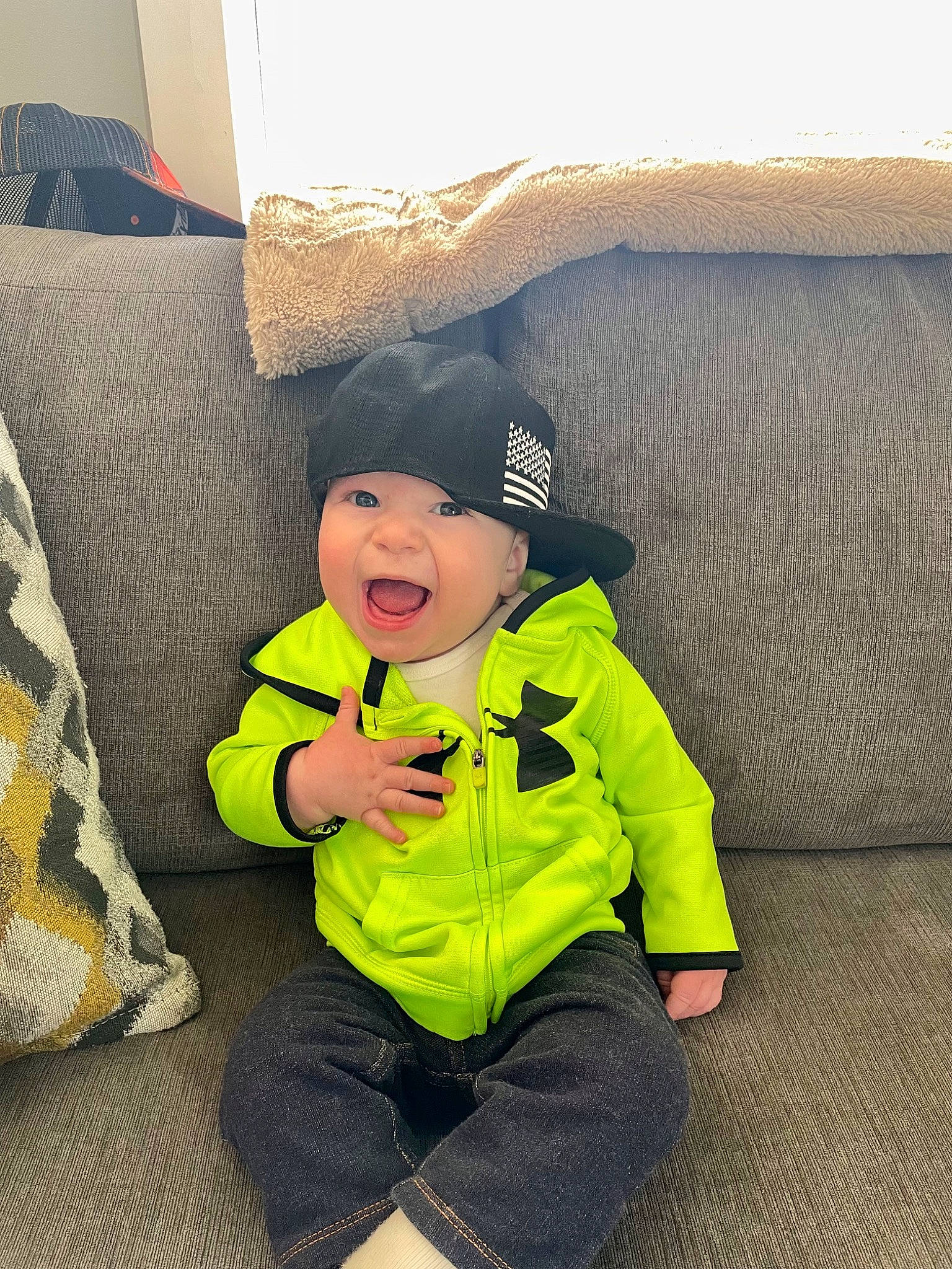 Elijah joined the competition — help win amazing prizes! baby, baby_toddler_clothing, cap, child, comfort, couch, flooring, fun, grass, happy, headwear, jacket, linens, outerwear, person, personal_protective_equipment, pillow, sitting, sleeve, smile