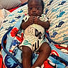 baby, infant, child, portrait, sitting, bed, blanket, pillow, whale_pattern, ocean_theme, onesie, socks, dark_skin, curly_hair, indoors, bedroom, cozy, colorful, face, photography
