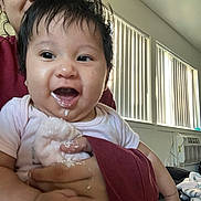 Everlee is registered to the contest to win money with this photo: adult, baby, caregiver, child, dark_hair, eyes, face, happy, holding, home, indoor, infant, milk, open_mouth, person, pink_shirt, plush_toy, portrait, smiling, window_blinds