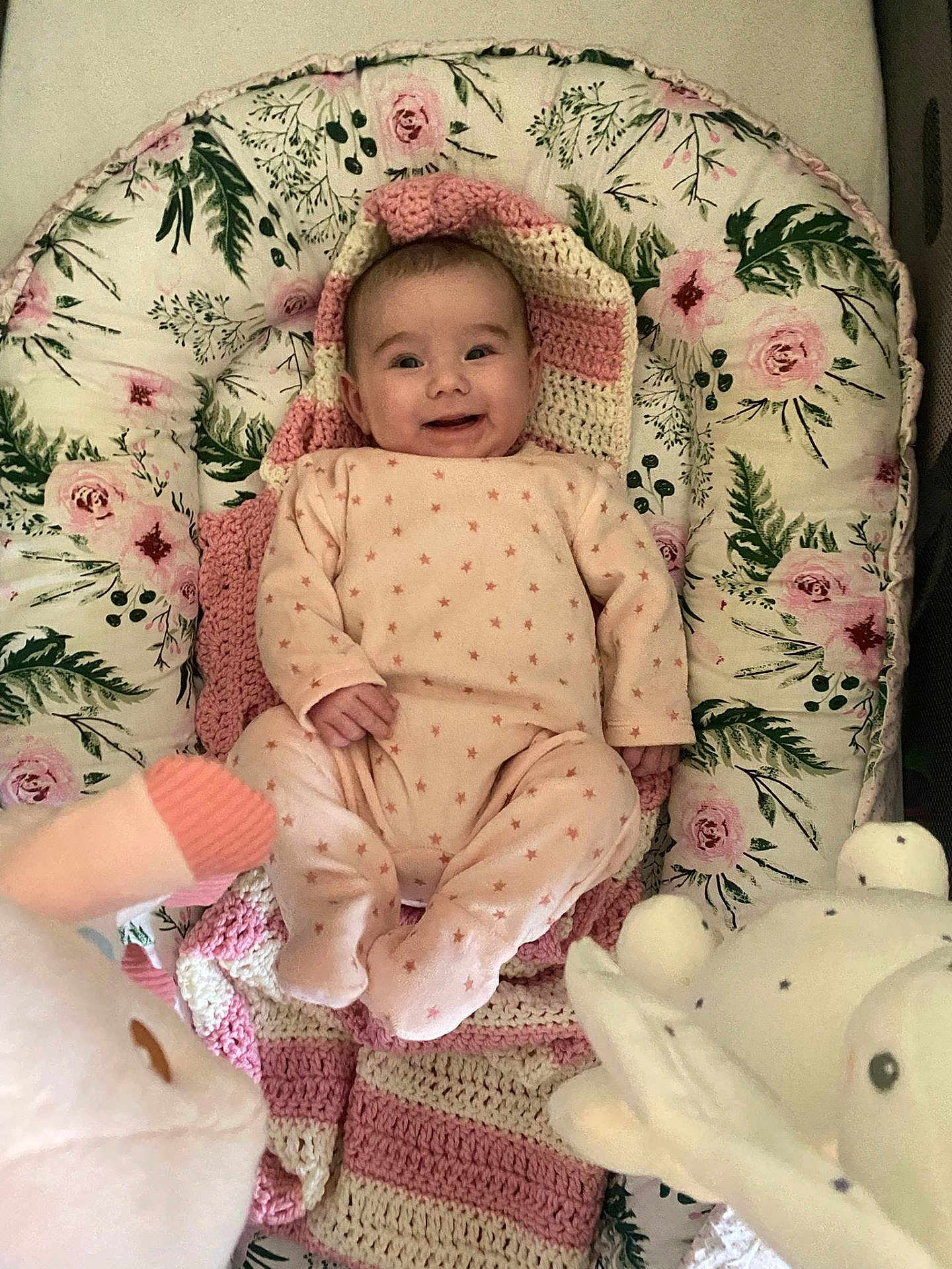 Mélina participe au concours pour gagner de l'argent avec cette photo : baby, infant, child, smiling, onesie, pink, floral_bedding, crochet_blanket, plush_toy, stuffed_animal, crib, bedding, cozy, portrait, lying_down, rosy_cheeks, hands, feet, nursery, soft_toy