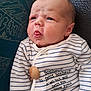 baby, infant, face, tongue, expression, striped_clothing, onesie, wooden_button, text_on_clothing, blue_stripes, cute, young_child, portrait, closeup, indoor, seated, fabric, texture, skin, person