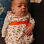 baby, infant, child, dress, cherry_pattern, orange_belt, couch, pillow, blue_pillow, indoor, person, young_child, sitting, cute, looking_up, hand, fabric, home, soft_lighting, portrait