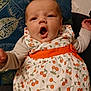 baby, infant, child, dress, cherry_pattern, orange_sash, cushion, blue_cushion, golden_leaf_design, mouth_open, expression, sitting, indoor, face, person, clothing, cute, young_child, portrait, fabric