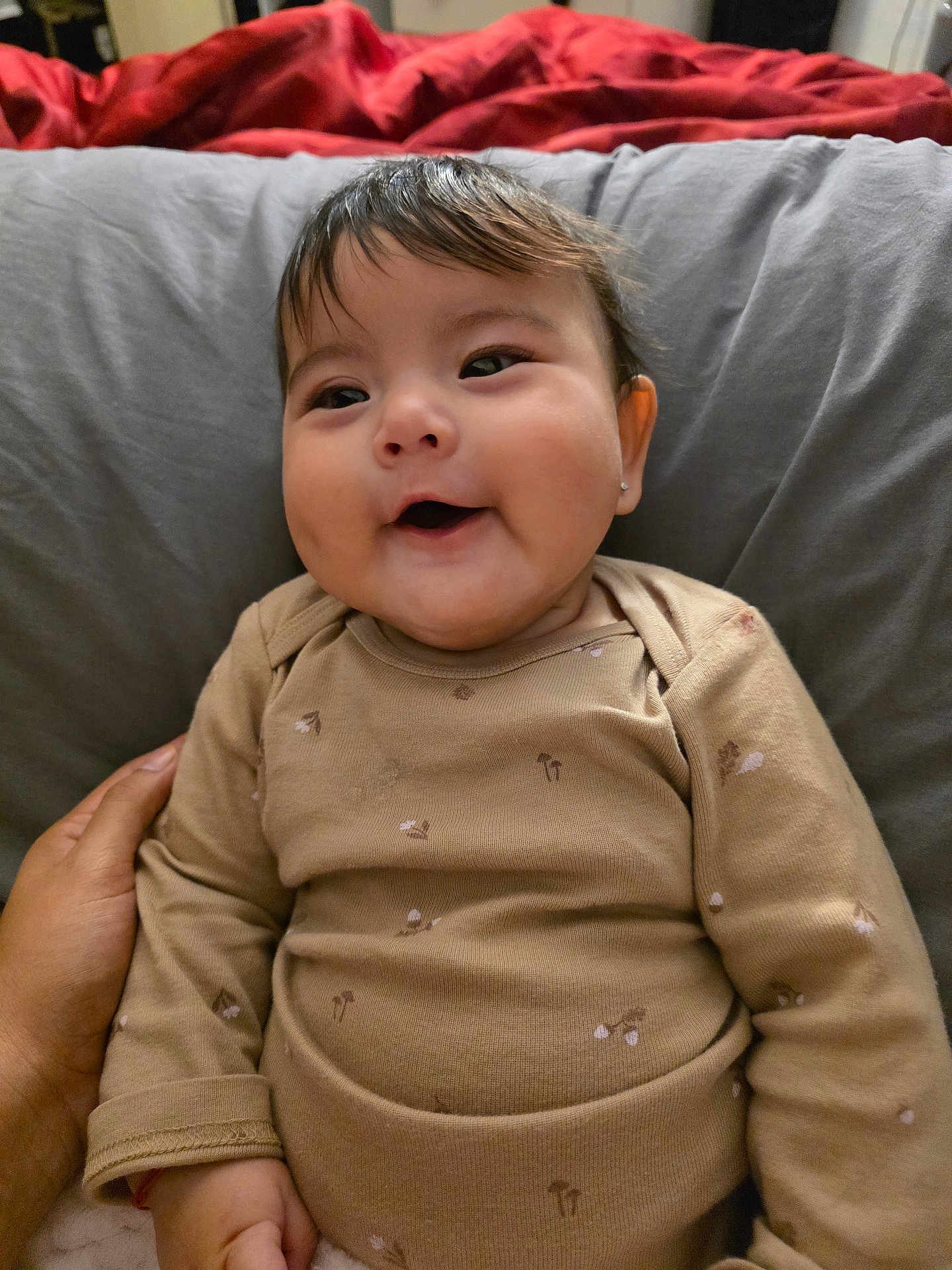 Carla joined the competition — help win amazing prizes! baby, child, smiling, onesie, beige_clothing, face, hand, pillow, blanket, indoor, person, happy, cute, head, portrait, infant, cozy, warm, resting, holding