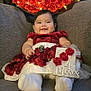 baby, infant, smiling, red_dress, white_tights, couch, flowers, roses, bouquet, lights, celebration, decor, cute, portrait, indoors, holding_sign, happy, child, sitting, cozy